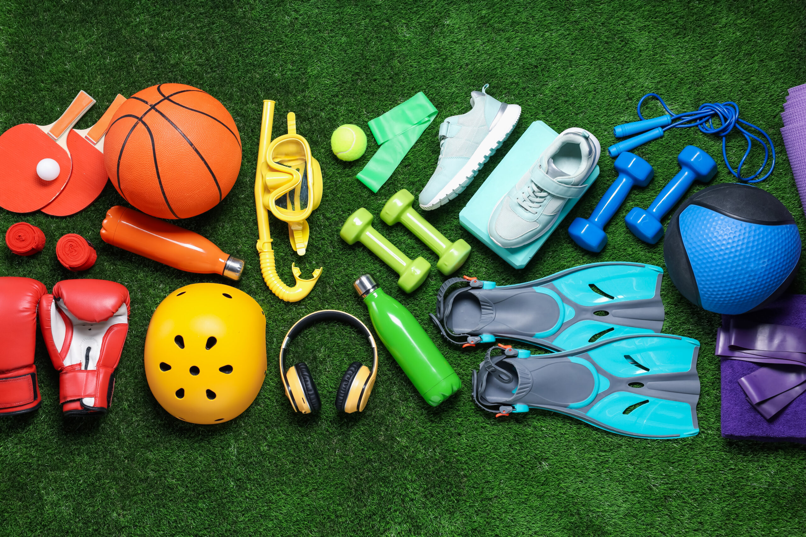 Different sports equipment, bottle and headphones on green grass, flat lay